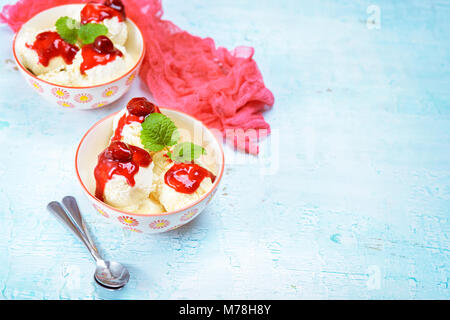 Vailla delizioso gelato alla crema con salsa di cherrry in due ciotole blu sul tavolo di legno. Spazio di copia Foto Stock