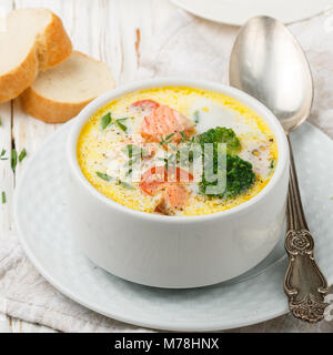 Chowder con trote e verdure - patate, carote, pomodori e broccoli in una ciotola bianco luminoso su un tavolo di legno Foto Stock