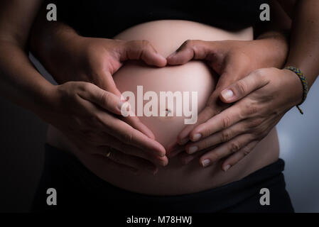 Gravidanza womans ventre con le mani del padre e della madre formando un cuore Foto Stock