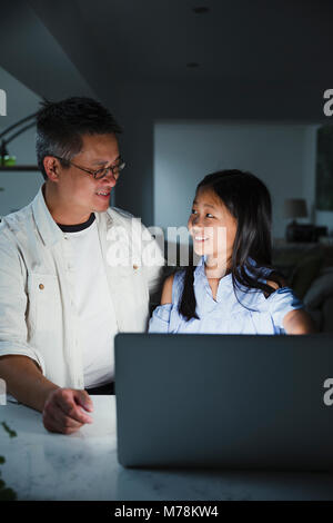 Bambina è ottenere aiuto da suo padre mentre facendo i compiti sul portatile a casa. Foto Stock