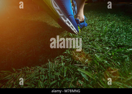 Uomo di jogging sul campo verde erba in scarpe blu. Close-up di messa a passo uomo Foto Stock