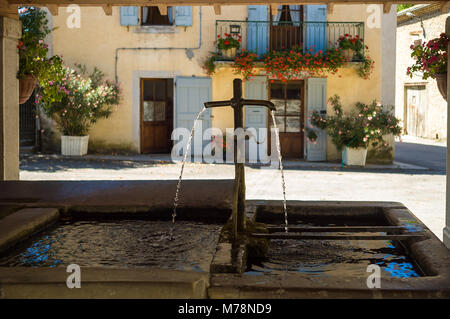 Una fontana in un antico lavatoio protetto da un tetto al centro di un quadrato in un piccolo villaggio francese con una tipica casa sullo sfondo decorat Foto Stock