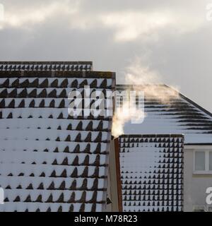 Il vapore da una ventola di riscaldamento si sposta oltre i tetti coperti di neve durante il freddo in Scozia, Regno Unito Foto Stock