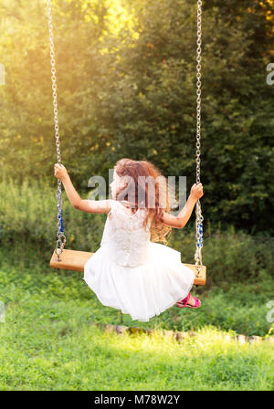 Felice bella ragazza seduta in altalena al giorno di estate, vista posteriore Foto Stock