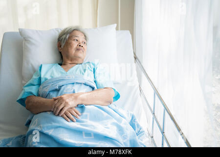 Asian premuto donna anziana paziente sdraiato sul letto guardando fuori dalla finestra in ospedale. Donna anziana pazienti è lieto recuperato dalla malattia. Foto Stock