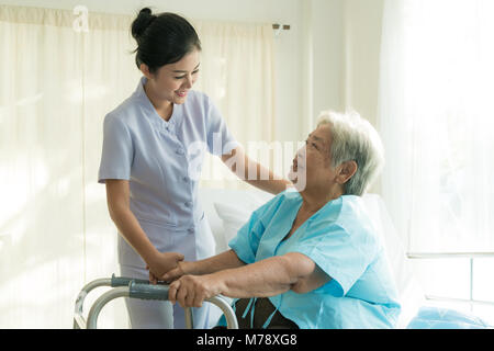 Giovani asiatici infermiera il supporto paziente anziano donna disabile in utilizzando walker in ospedale. Pazienti anziani il concetto di cura. Foto Stock