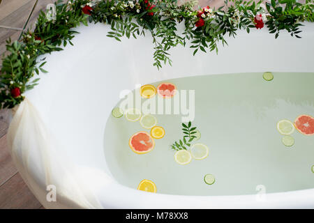 Latte acqua nella vasca da bagno, che nuotare citrus: lime, limone e pompelmo.La cura della pelle e il rilassamento bagno riempito con acqua e decorate con fiori Foto Stock