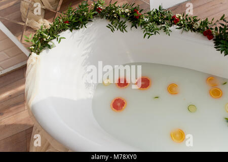 Latte acqua nella vasca da bagno, che nuotare citrus: lime, limone e pompelmo.La cura della pelle e il rilassamento bagno riempito con acqua e decorate con fiori Foto Stock