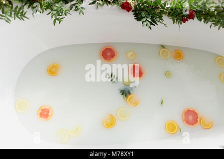 Latte acqua nella vasca da bagno, che nuotare citrus: lime, limone e pompelmo.La cura della pelle e il rilassamento bagno riempito con acqua e decorate con fiori Foto Stock