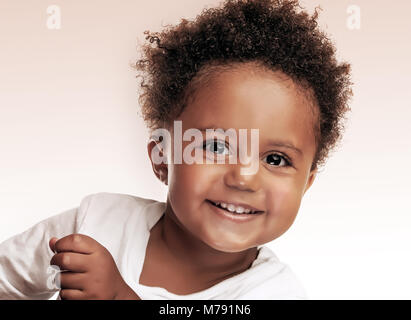 Closeup ritratto di un piccolo grazioso african american boy isolato beige su sfondo bianco, dolce bambino divertirsi in studio, allegria e spensieratezza Foto Stock