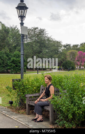 Una femmina di turista caucasica seduto su una panca in legno nei Giardini Botanici di Singapore. Foto Stock