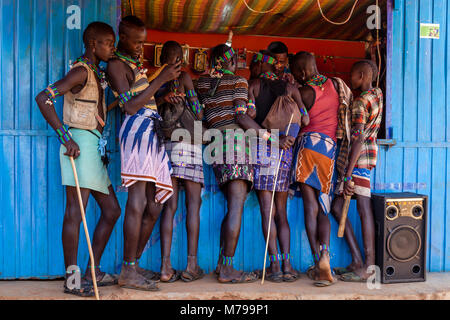 Giovani Hamar uomini al di fuori di un telefono cellulare (telefono cellulare) negozio durante la loro visita settimanale al mercato tribale In Dimeka, Valle dell'Omo, Etiopia Foto Stock