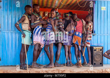 Giovani Hamar uomini al di fuori di un telefono cellulare (telefono cellulare) negozio durante la loro visita settimanale al mercato tribale In Dimeka, Valle dell'Omo, Etiopia Foto Stock