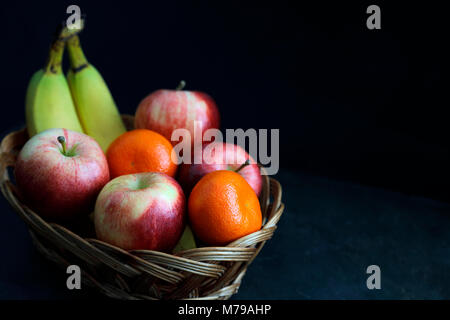 Cibo scuro - Chiaroscuro frutta mista nel cesto di vimini con sfondo scuro con spazio copia a destra Foto Stock