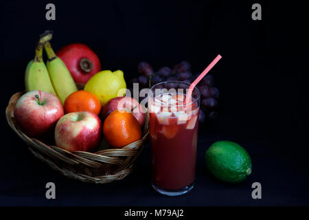 Cibo scuro - Chiaroscuro frutta mista nel cesto di vimini con punch alla frutta con sfondo scuro e spazio di copia Foto Stock