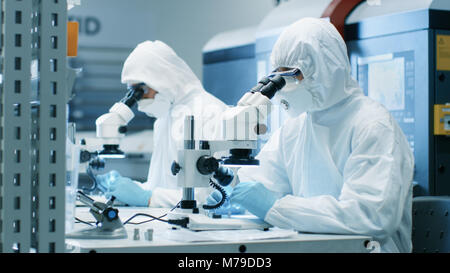 Due ingegneri/ scienziati/ tecnici in sterili per cleanroom utilizzare tute di microscopi per l'organo di regolazione e di ricerca. Essi lavorano in un laboratorio moderno Foto Stock