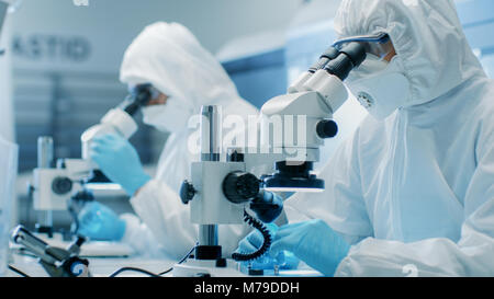 Due ingegneri/ scienziati/ tecnici in sterili per cleanroom utilizzare tute di microscopi per l'organo di regolazione e di ricerca. Essi lavorano in un laboratorio moderno Foto Stock