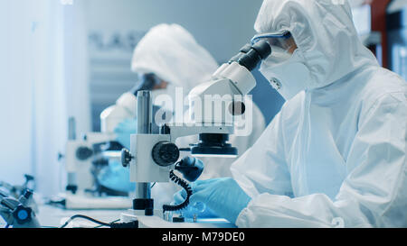 Due ingegneri/ scienziati/ tecnici in sterili per cleanroom utilizzare tute di microscopi per l'organo di regolazione e di ricerca. Essi lavorano in un laboratorio moderno Foto Stock