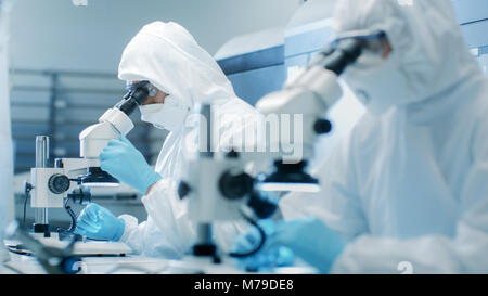 Due ingegneri/ scienziati/ tecnici in sterili per cleanroom di controllo adatta per la produzione di macchine di lavoro e utilizzare microscopi per la regolazione del componente Foto Stock