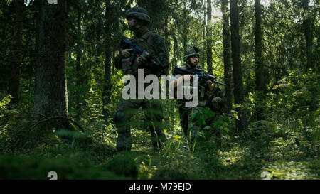 Squadra di cinque completamente attrezzata soldati a una ricognizione missione militare. Si muovono in formazione attraverso la densa foresta. Foto Stock