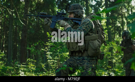 Squadra di completamente accessoriate soldati in camuffamento su una ricognizione missione militare, puntando fucili. Si muovono in formazione attraverso la densa foresta. Foto Stock