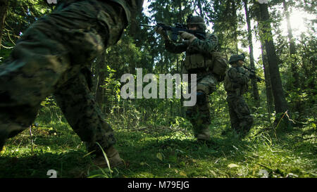 Squadra di completamente accessoriate soldati in camuffamento su una ricognizione missione militare, puntando fucili. Si muovono in formazione attraverso la densa foresta. Foto Stock