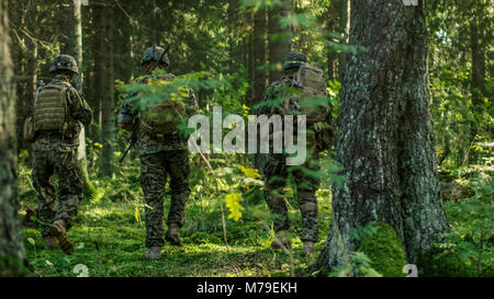 Squadra di cinque completamente equipaggiato i soldati in camuffamento su una ricognizione missione militare, fucili a canna rigata in posizione di tiro. Si muovono attraverso la foresta. Foto Stock