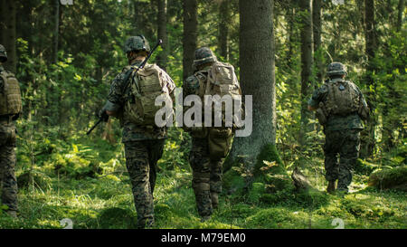 Squadra di cinque completamente equipaggiato i soldati in camuffamento su una ricognizione missione militare, fucili a canna rigata in posizione di tiro. Si muovono attraverso la foresta. Foto Stock