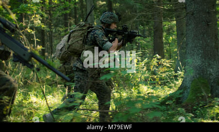 Completamente accessoriate soldati indossano uniformi di mimetizzazione Nemico, fucili in posizione di tiro. Operazione militare in azione, Squad Esecuzione di foresta. Foto Stock