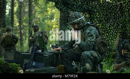 Militare Base di staging, capo ingegnere militare utilizza Radio Walkie-Talkie e grado dell'esercito, portatile. Le squadre risiede nel mimetizzata tenda mentre è in missione. Foto Stock