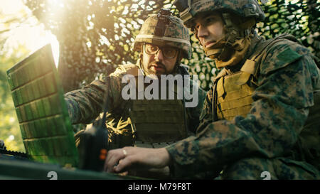 Militare Base di staging, funzionario dà gli ordini al Chief Engineer, essi utilizzare la radio e il grado dell'esercito, portatile. Essi sono in mimetizzata tenda in una foresta. Foto Stock