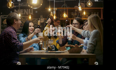 Diversi gruppi di amici festeggiare con un brindisi e il Clink sollevato bicchieri con bevande varie nella celebrazione. Bella Giovani Divertirsi Foto Stock