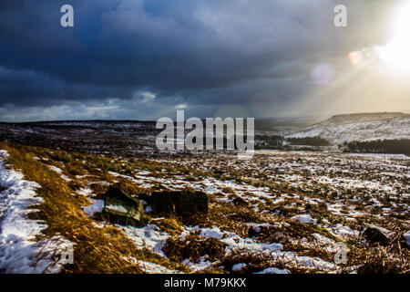 Raggi di sole proveniente attraverso le nubi in un giorno di neve, Burbage, Peak District Foto Stock