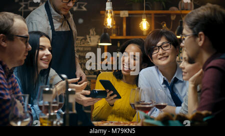 Nel Bar cameriere detiene il pagamento con carta di credito la macchina e bella donna paga per il suo ordine con Contactless Telefono Mobile sistema di pagamenti. Foto Stock