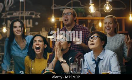 Diversi gruppi di amici Orologi TV in Sporstbar. Il loro punteggio di squadra il traguardo e vince. Giovani allegria. Foto Stock