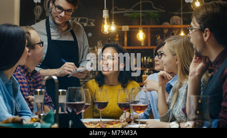 Nel Bar/Ristorante cameriere prende fine da un variegato gruppo di amici. Bella gente bere vino e di avere un buon tempo in questo elegante luogo. Foto Stock