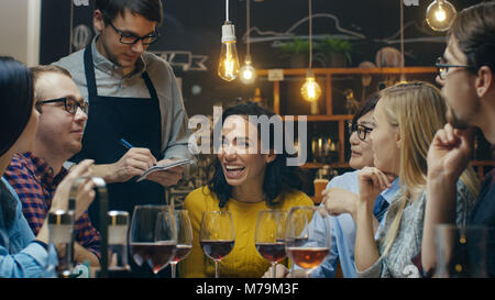 Nel Bar/Ristorante cameriere prende fine da un variegato gruppo di amici. Bella gente bere vino e di avere un buon tempo in questo elegante luogo. Foto Stock