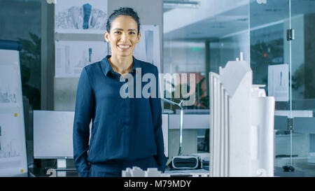 Femmina progettista architettonico funziona su un modello di un quartiere di una città con edifici, parchi e un proprio ecosistema. Sorride. Bella Donna elegante Foto Stock