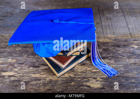 Graduazione mortarboard sulla parte superiore della pila di libri su abstract Sfondo legno Foto Stock