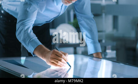 Senior Engineer architettonico richiama Building Concept su una Tavoletta Grafica Display touchscreen verticale tabella. Pulire Ufficio minimalista, muro di cemento Foto Stock