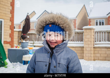 Giovane ragazzo giocare nella neve nel loro giardino sul retro Foto Stock