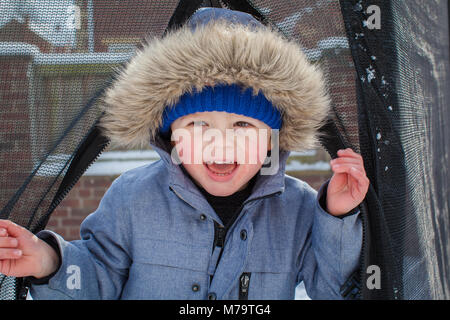 Giovane ragazzo giocare nella neve nel loro giardino sul retro Foto Stock