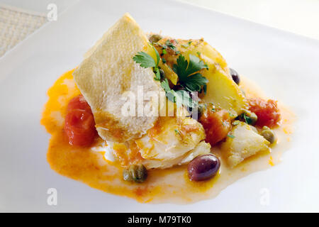 Fetta di merluzzo cotto alla griglia e in padella con una salsa di pomodori ciliegini, olive e capperi, un pizzico di prezzemolo, olio e sale. Foto Stock