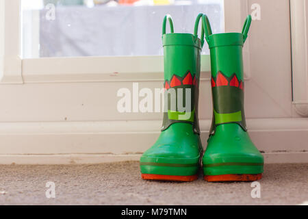 Giovani bambini wellies colorati seduto su un tappeto mediante la porta posteriore Foto Stock