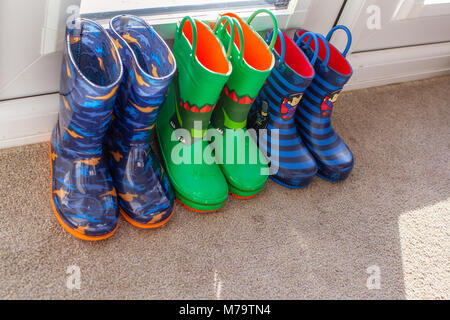 Giovani bambini wellies colorati seduto su un tappeto mediante la porta posteriore Foto Stock