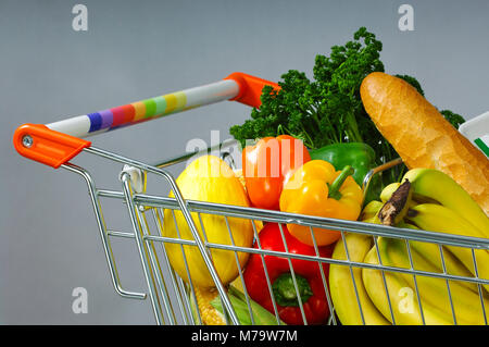 Carrello spesa piena di colorati di verdure, frutta e pane isolato su sfondo grigio Foto Stock