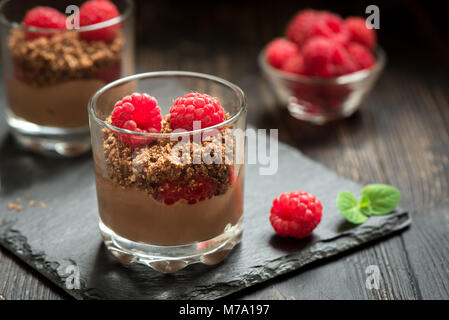 Dolce al cioccolato in bicchieri con lamponi. Mousse al cioccolato o budini nella porzione occhiali con frutti di bosco freschi, copia dello spazio. Foto Stock