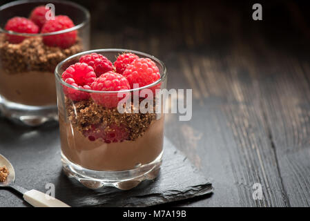 Dolce al cioccolato in bicchieri con lamponi. Mousse al cioccolato o budini nella porzione occhiali con frutti di bosco freschi, copia dello spazio. Foto Stock