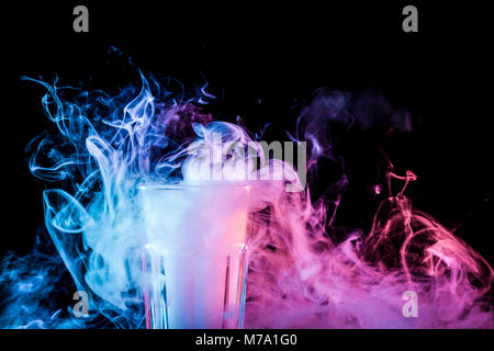 Close up di un vetro trasparente riempita con un cloud da un rosa vape fuma e sorge su un isolato nero lo sfondo Foto Stock