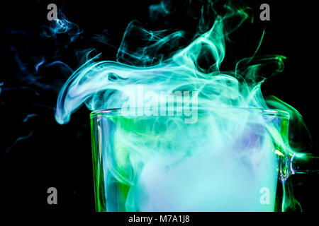 Close up di un vetro trasparente per la birra riempita con un cloud da un verde vape fuma e sorge su un isolato nero lo sfondo Foto Stock